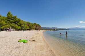 A beach with clear shallow water, trees, and a few people.