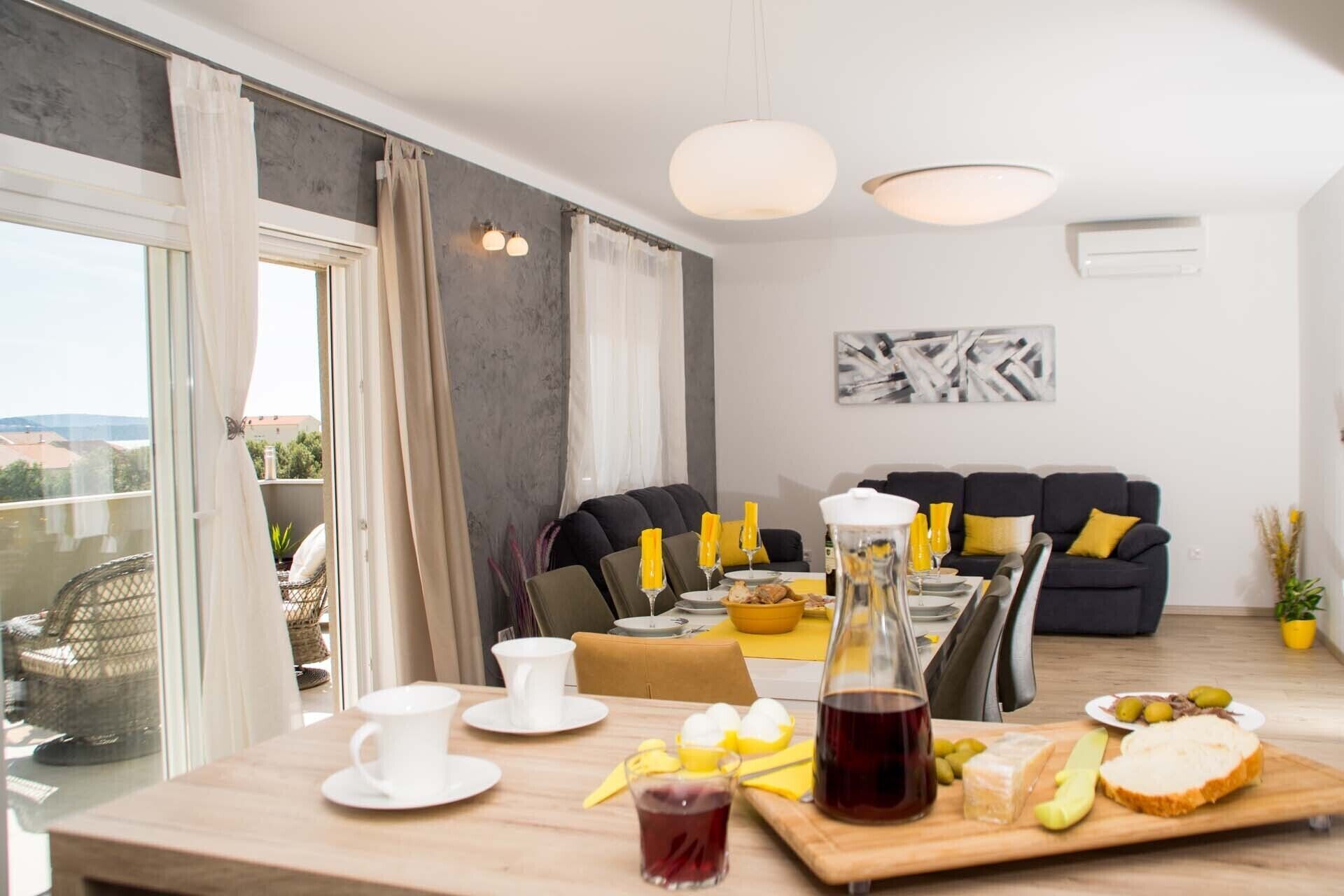 A dining area with a table set for two, a sofa, and a balcony with a view.