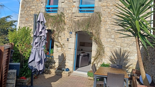 Ein Steinhaus mit einer Terrasse, die einen Tisch, Stühle, einen Sonnenschirm und einen Blumentopf zeigt.