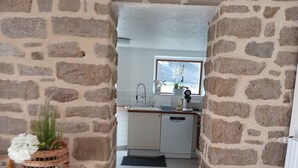Ein steinernes Bogenportal führt zu einer Küche mit weißen Schränken, einem Fenster und einem kleinen Tisch mit einem Korbwäscher und weißen Blumen.