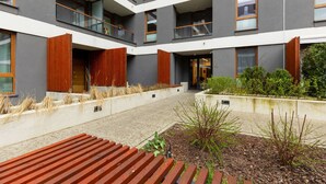 Un bâtiment moderne doté de nombreux balcons, d’une cour avec des bancs en bois et d’un jardin aménagé.