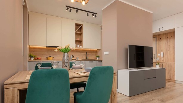 Une cuisine moderne avec un coin repas, des meubles en bois, un téléviseur et une petite plante.