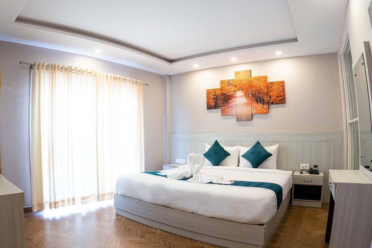 Une chambre d’hôtel moderne avec un grand lit, une table de chevet, une lampe de chevet, une œuvre d’art accrochée au mur et un tapis rouge d’accueil.