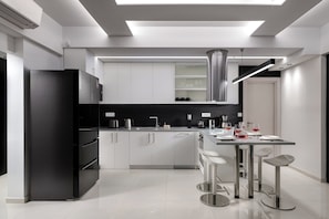 Une cuisine moderne avec un réfrigérateur noir, des appareils en acier inoxydable, des armoires blanches et un coin bar avec des tabourets.