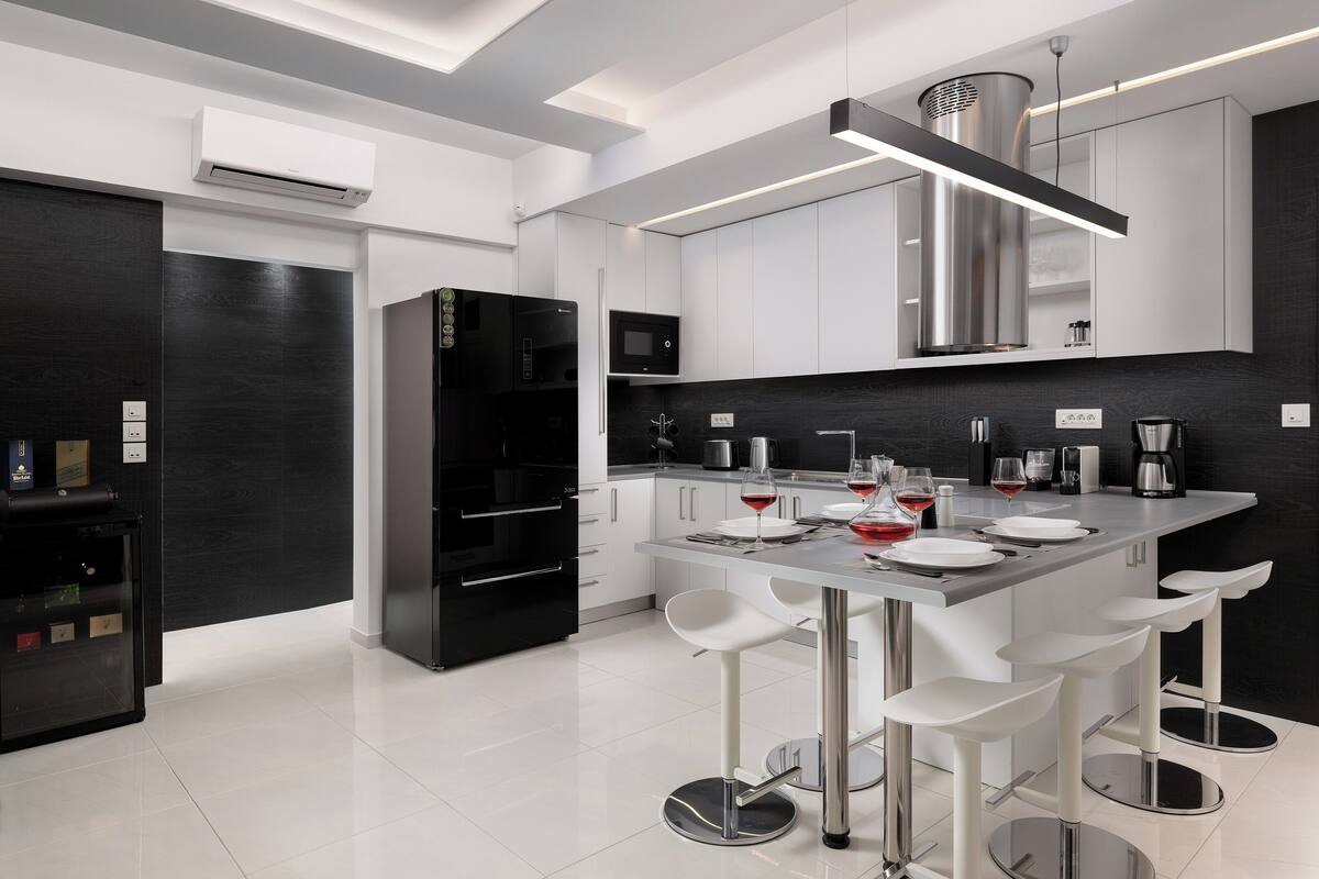 A modern kitchen with a central island, bar stools, and a black refrigerator.