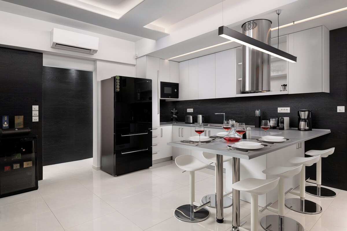 A modern kitchen with a central island, bar stools, and a black refrigerator.