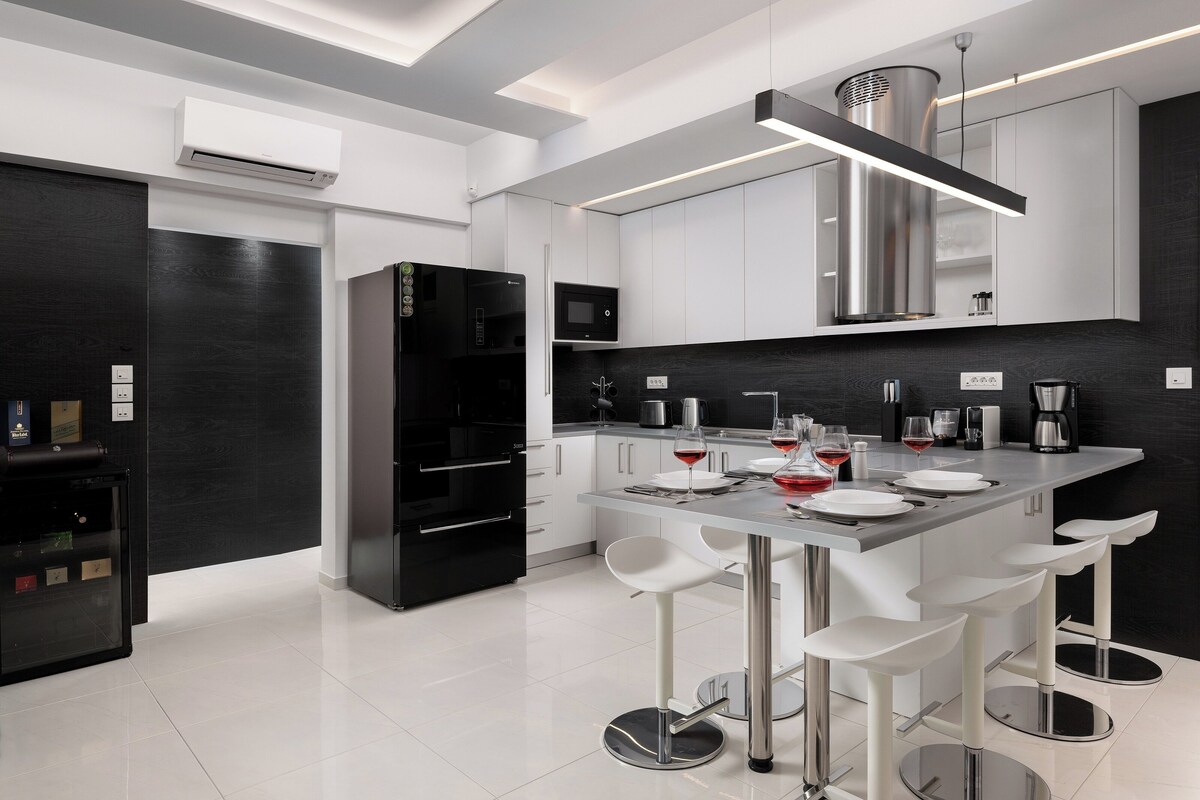 A modern kitchen with a central island, bar stools, and a black refrigerator.