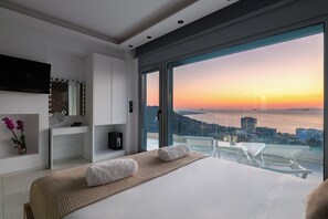 Quarto moderno com uma cama grande, uma toucador com espelho e vista para o pôr do sol sobre a água.