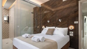 Quarto de hotel moderno com uma cama grande, cabine de chuveiro envidraçada e uma parede de destaque em madeira.