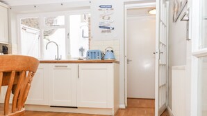 A kitchen with white cabinets, a wooden chair, and a blue kettle on the counter. - Sea Beach Cottage (Eastbourne)