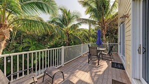 A wooden deck with outdoor furniture, surrounded by palm trees and a white railing.