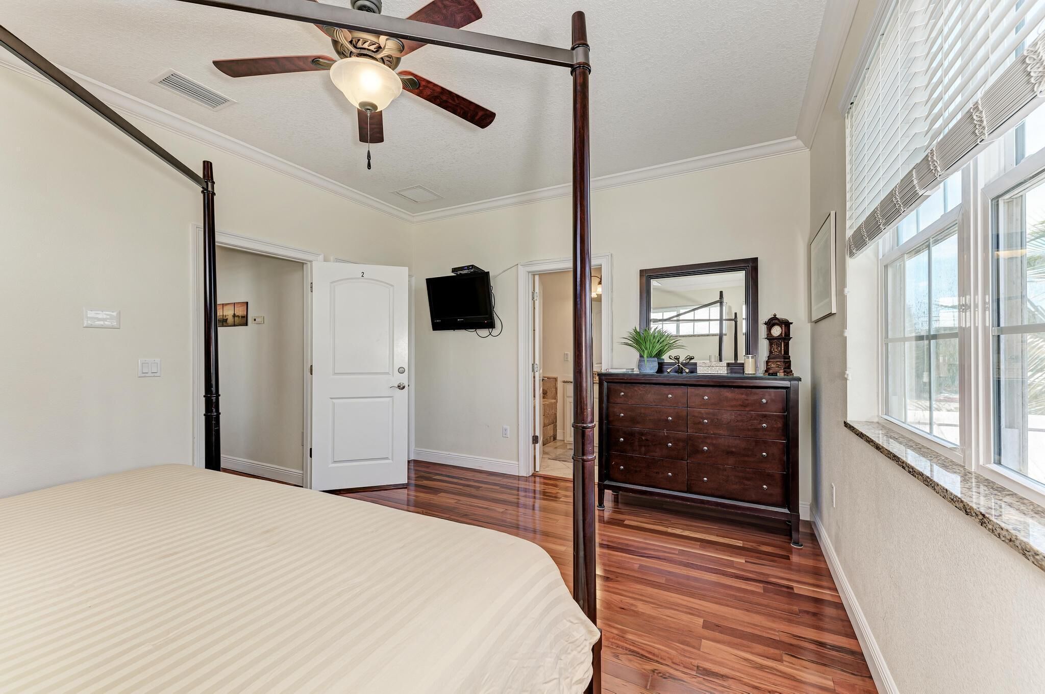 A bedroom with a bed, a ceiling fan, a dresser, a mirror, and a window.