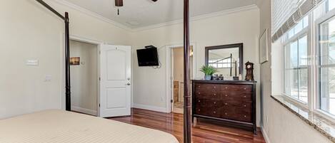 A bedroom with a bed, a ceiling fan, a dresser, a mirror, and a window.