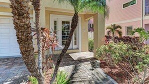 A residential building with a garage, palm trees, and a paved walkway.