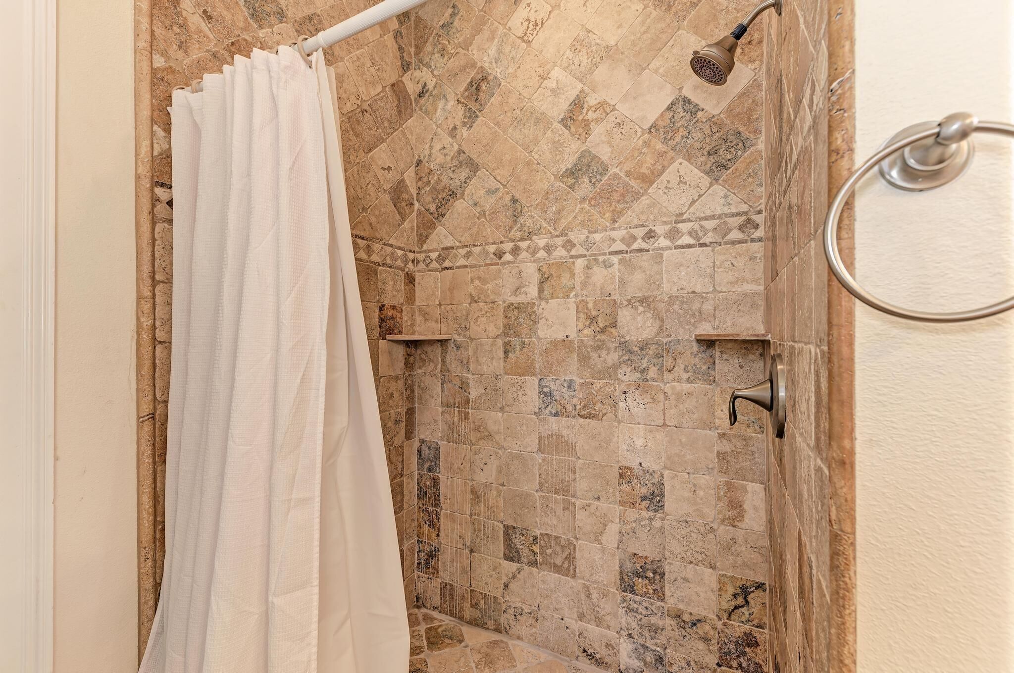 A shower area with a tiled wall, a showerhead, and a curtain.