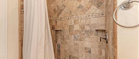A shower area with a tiled wall, a showerhead, and a curtain.