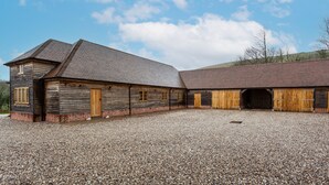 Un ampio edificio in stile rustico a forma di fienile, con diverse porte e finestre, un vialetto sterrato e cielo sereno.