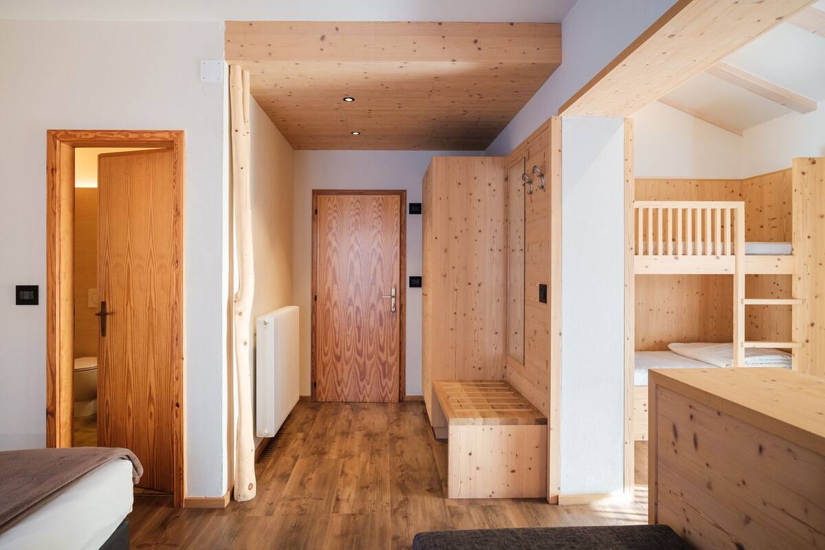 A compact room with a wooden floor, a bunk bed, a wooden wardrobe, and a door leading to another room.