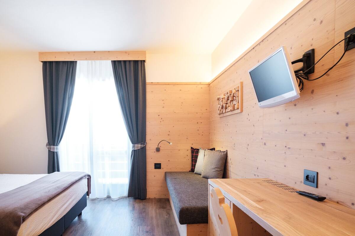 A modern hotel room with a wooden wall, a bed, a desk, and a TV mounted on the wall.