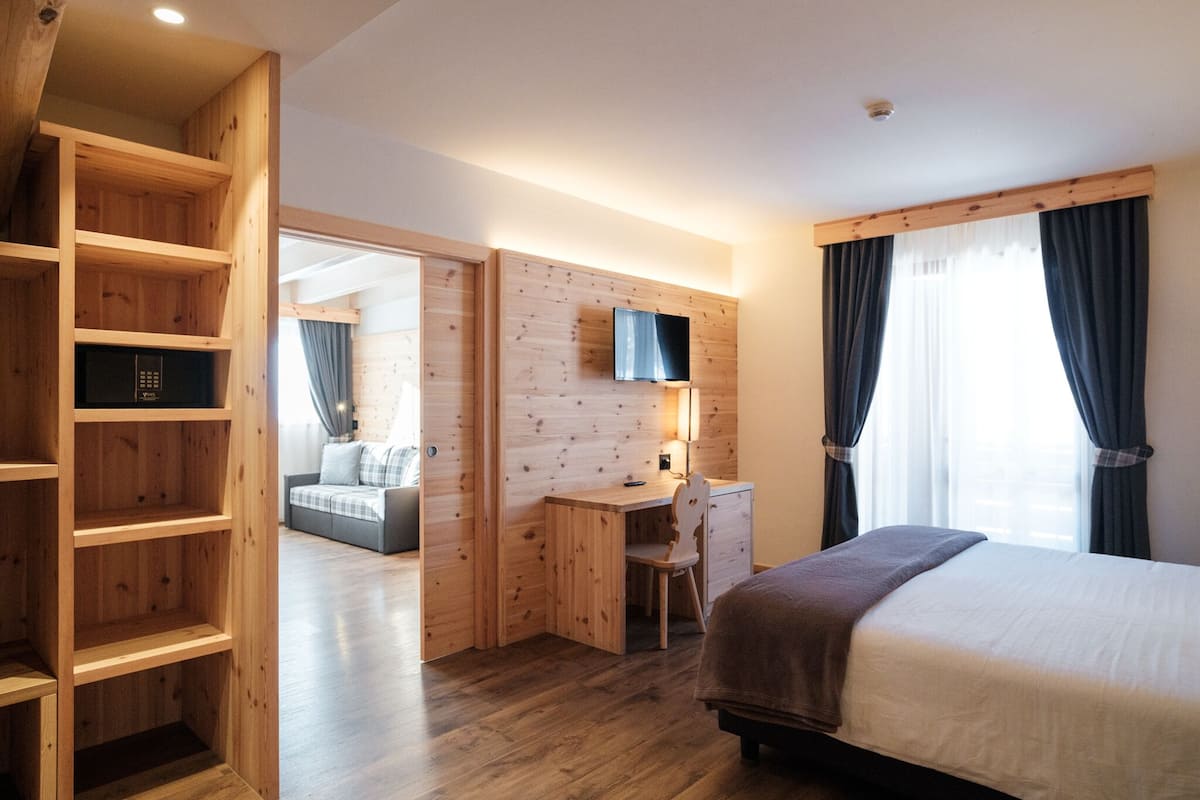A modern hotel room with a wooden desk, a bed, a TV, and a large window with curtains.