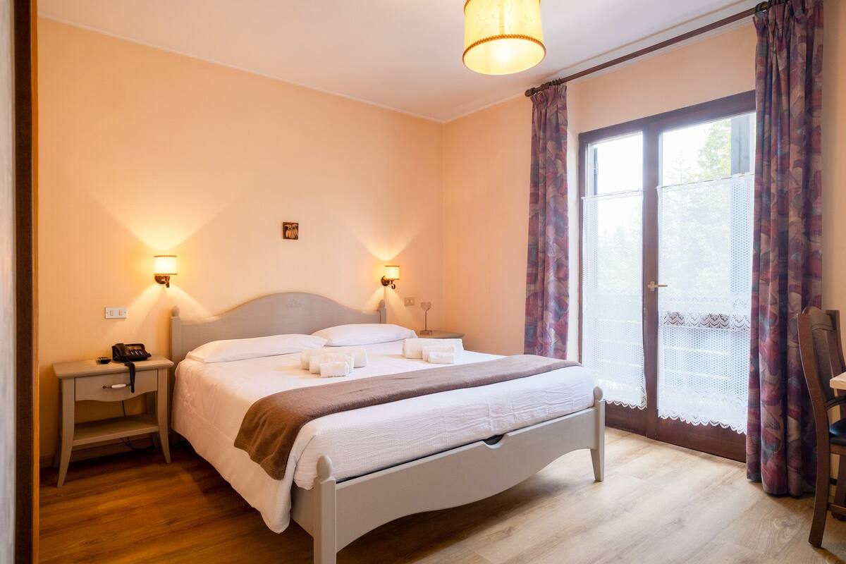 A bedroom with a bed, bedside lamps, a nightstand, and a window with curtains.
