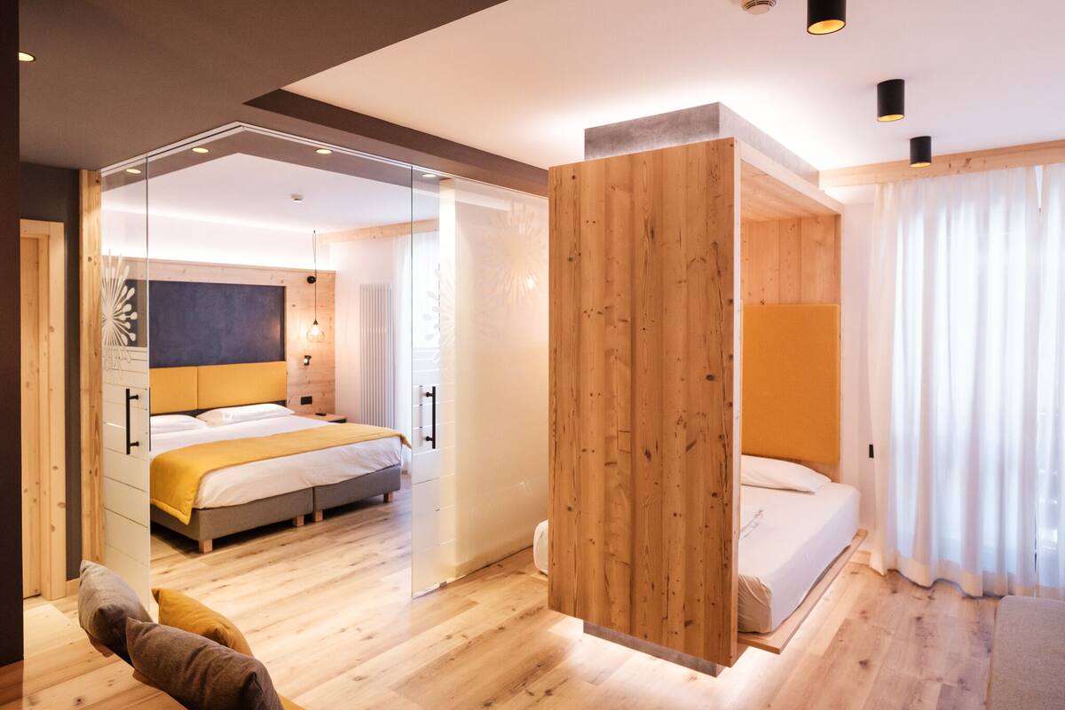 A modern hotel room with a large bed, a wooden accent wall, and a glass partition.