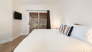 Une chambre dotée d’un grand lit, d’un ventilateur de plafond, d’un téléviseur fixé au mur et d’une porte coulissante avec des stores.