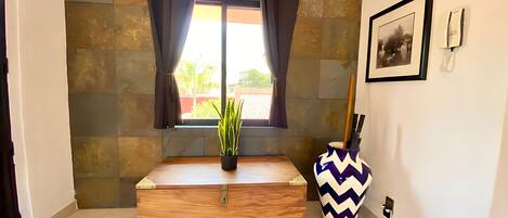A room with a wooden chest, a potted plant, a decorative vase, and a window with curtains.