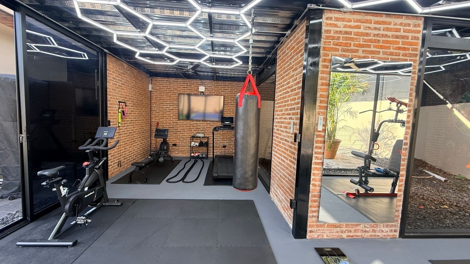 A gym with a brick wall, a punching bag, a treadmill, and exercise equipment.