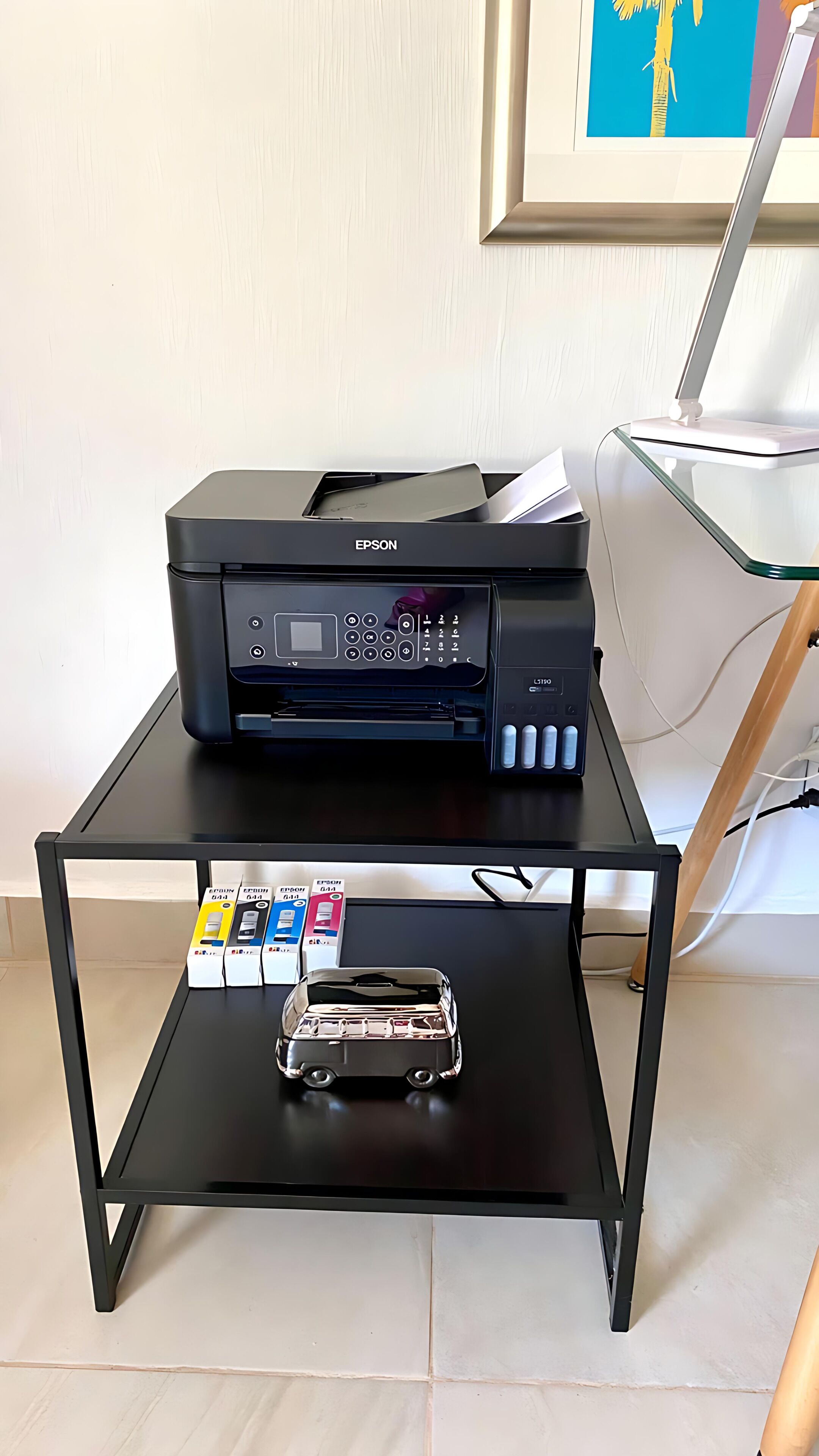 A black Epson printer on a black table with a small toy car and printer ink cartridges.