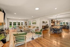 A spacious living room with a large sofa, a dining area with a wooden table, and a kitchen with modern appliances.