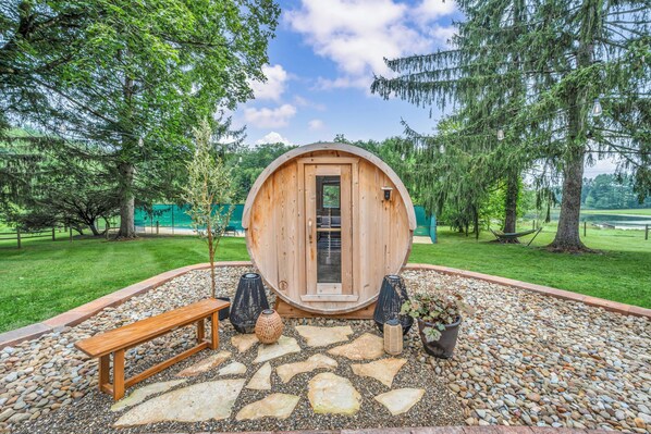 A wooden cabin with a door, surrounded by a stone patio, a bench, and potted plants.