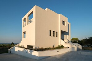 A modern two-story building with a flat roof, large windows, and a staircase leading to the entrance.