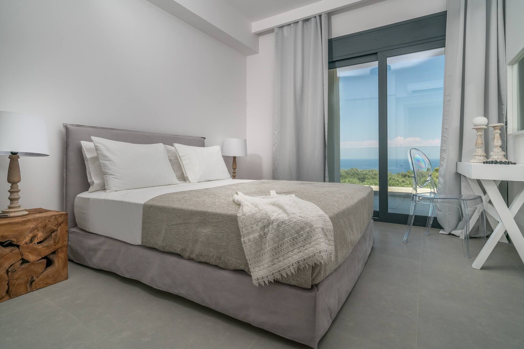 Une chambre moderne avec un lit, des lampes de chevet, une table de chevet en bois et une vue sur l’extérieur grâce à de grandes fenêtres.