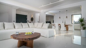 A modern living room with a large white sectional sofa, a wooden coffee table, and a dining area with white chairs. - Bianca Luxury Villa - Private Pool (Zakynthos)