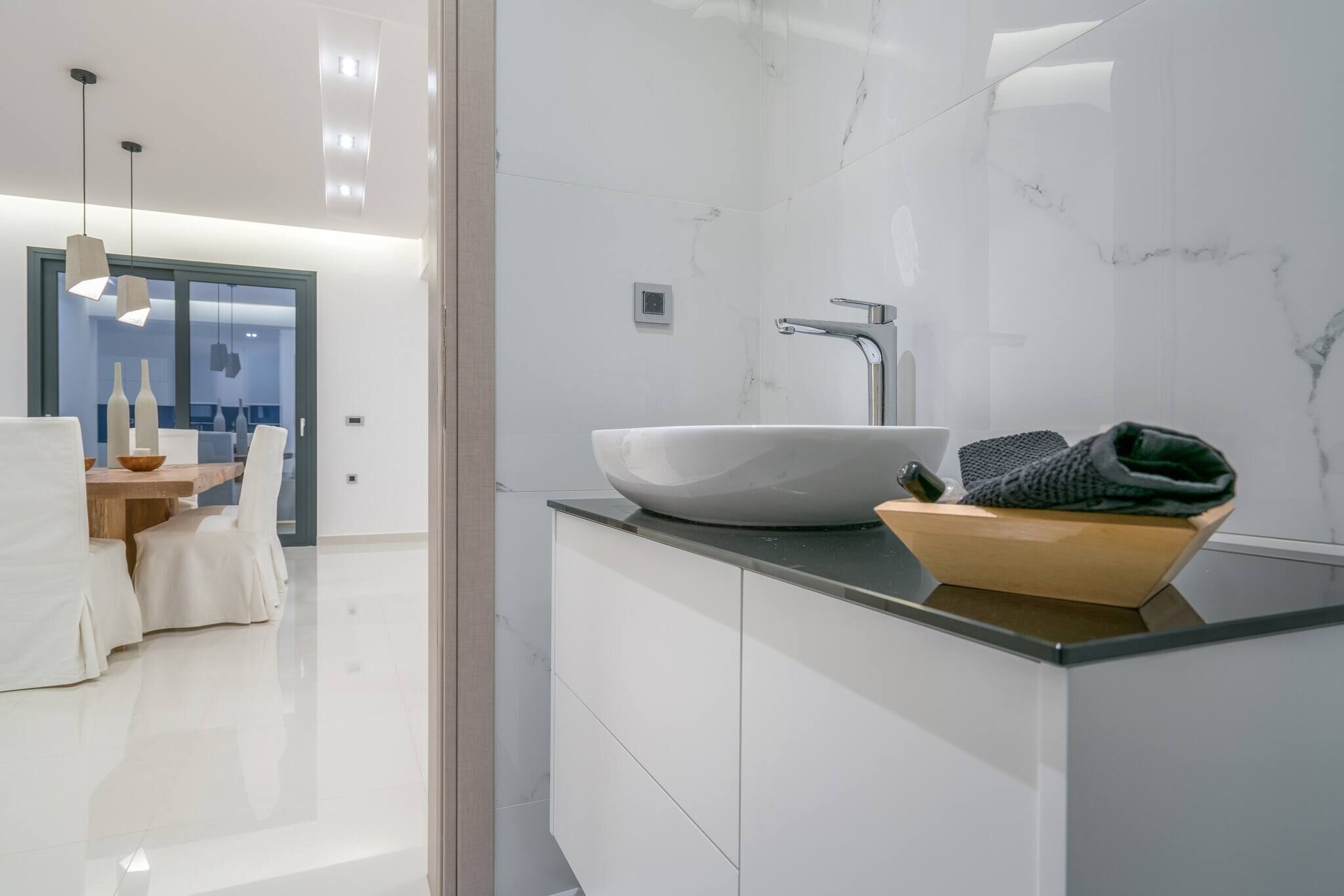 Une salle de bain moderne avec un lavabo en marbre blanc, un bol en bois et une serviette.