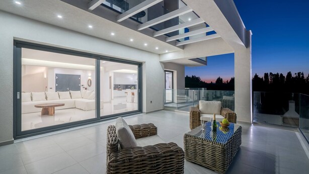 A modern outdoor living area with a glass balustrade, wicker furniture, and a flat-screen TV. - Bianca Luxury Villa - Private Pool (Zakynthos)
