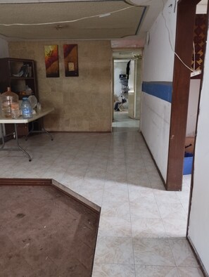 Un pasillo con suelo de baldosas, una mesa con botellas de agua y una puerta que da a otra habitación.