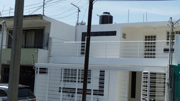 Kaksikerroksinen rakennus, jonka julkisivu on valkoinen, katolla on näkyvä vesisäiliö ja sisäänkäynti on portilla varustettu.