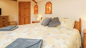 A bedroom with a floral bedspread, wooden headboard, and two wall-mounted lamps. - The Hideaway (St Austell)
