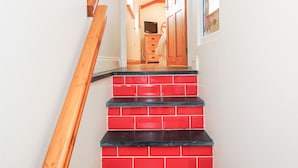 A staircase with red and black steps leading to a room with wooden beams and a television. - The Hideaway (St Austell)