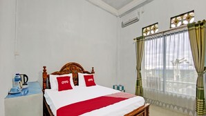 A hotel room with a wooden bed, white bedding, and a red throw. There is a window with curtains and a view of palm trees. - OYO 91927 Homestay Kebun (Kupang)