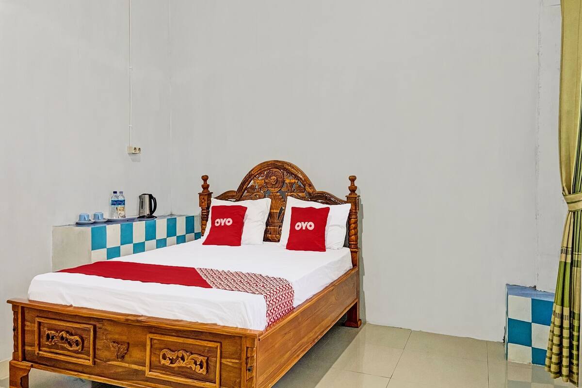 A wooden bed with a checkered headboard, white bedding, and red pillows with "OYO" branding.