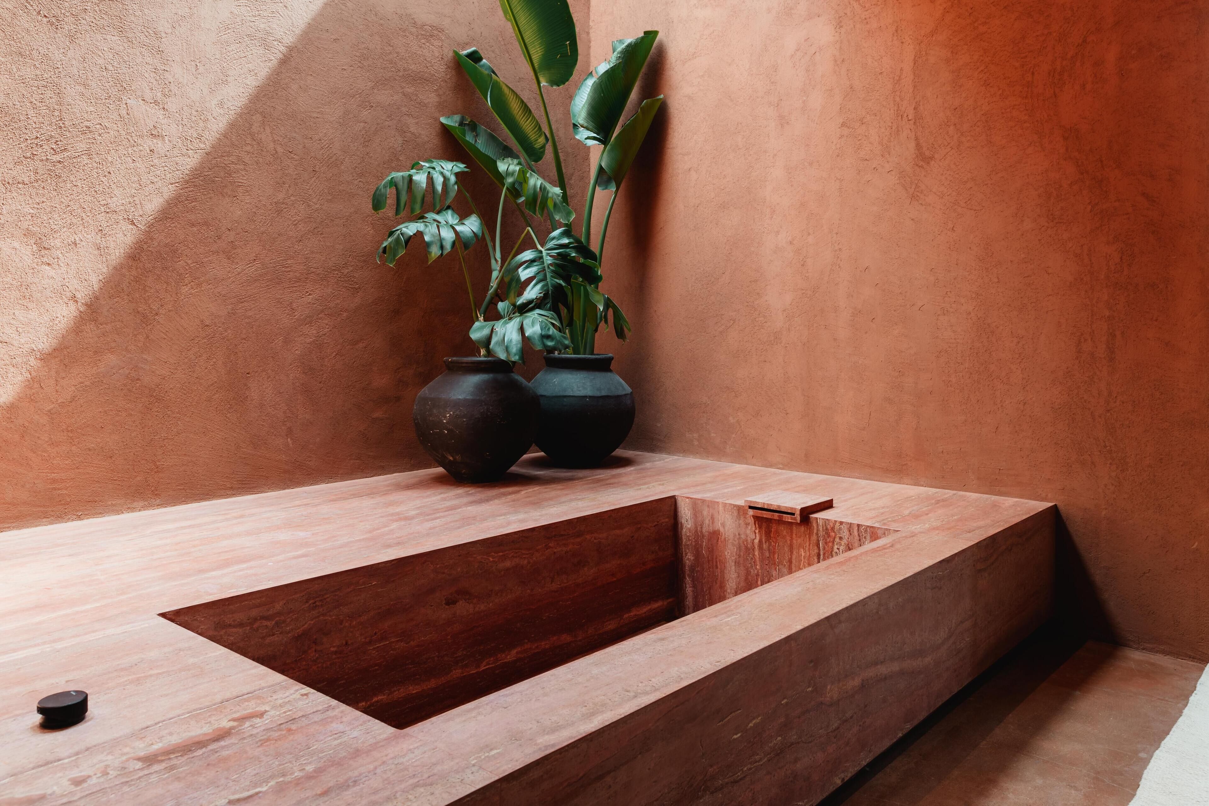Een moderne badkamer met een houten wasbak, twee donkere vazen met planten, en een structuurwand.