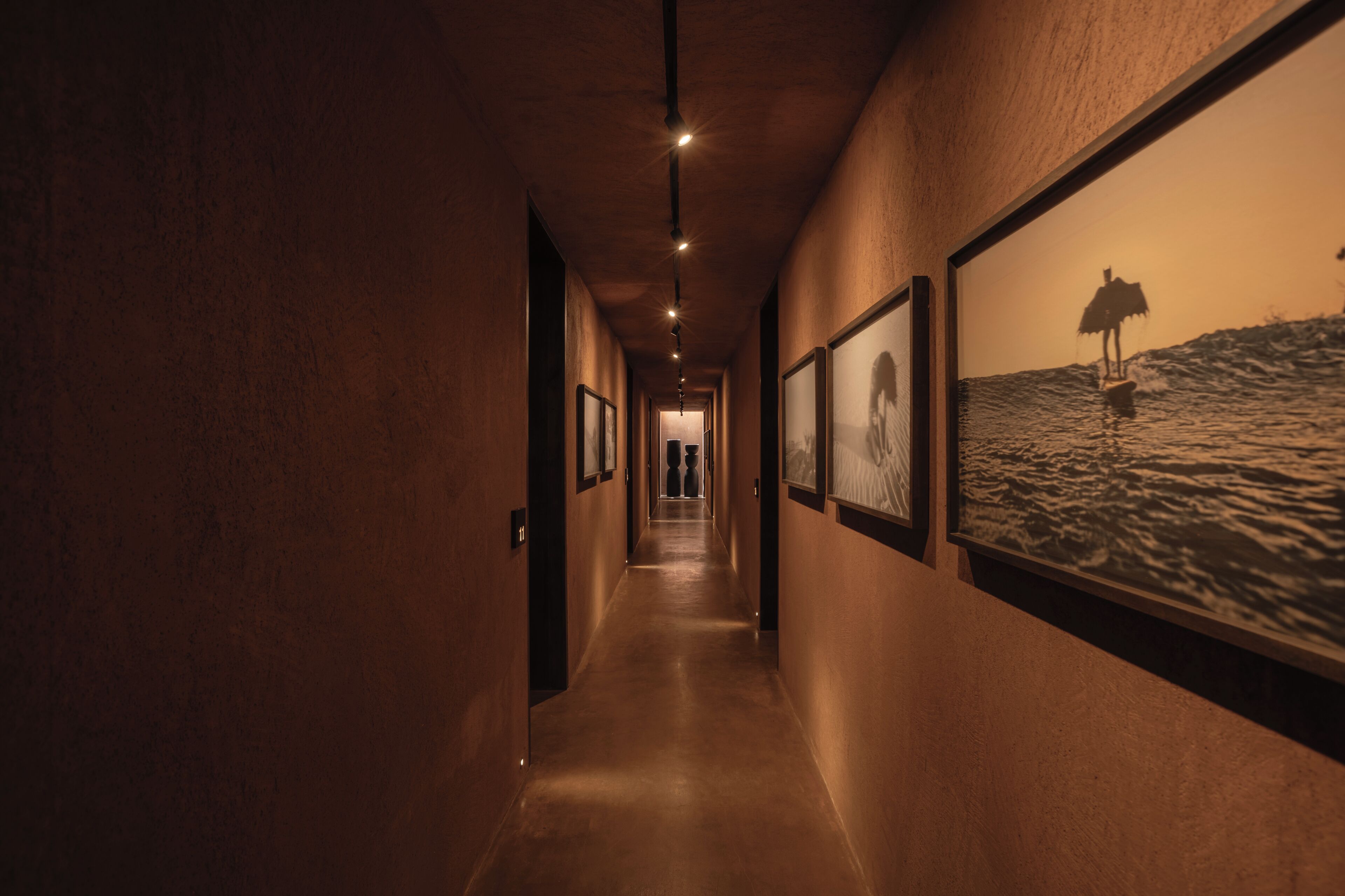 A hallway with framed pictures on the walls, a ceiling light, and a door at the end.