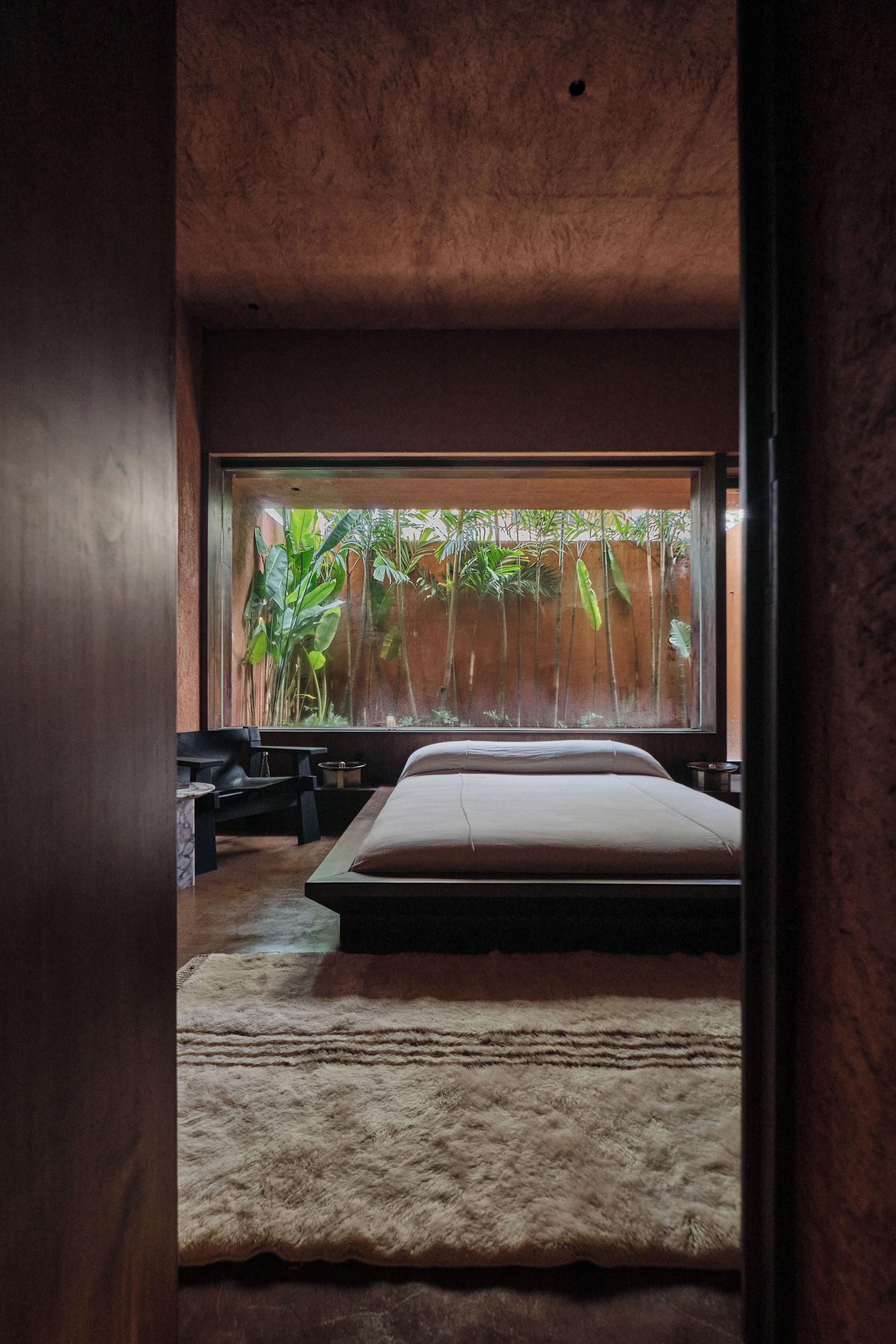 Un dormitorio con un ventanal grande, una cama, una mesita y una silla.