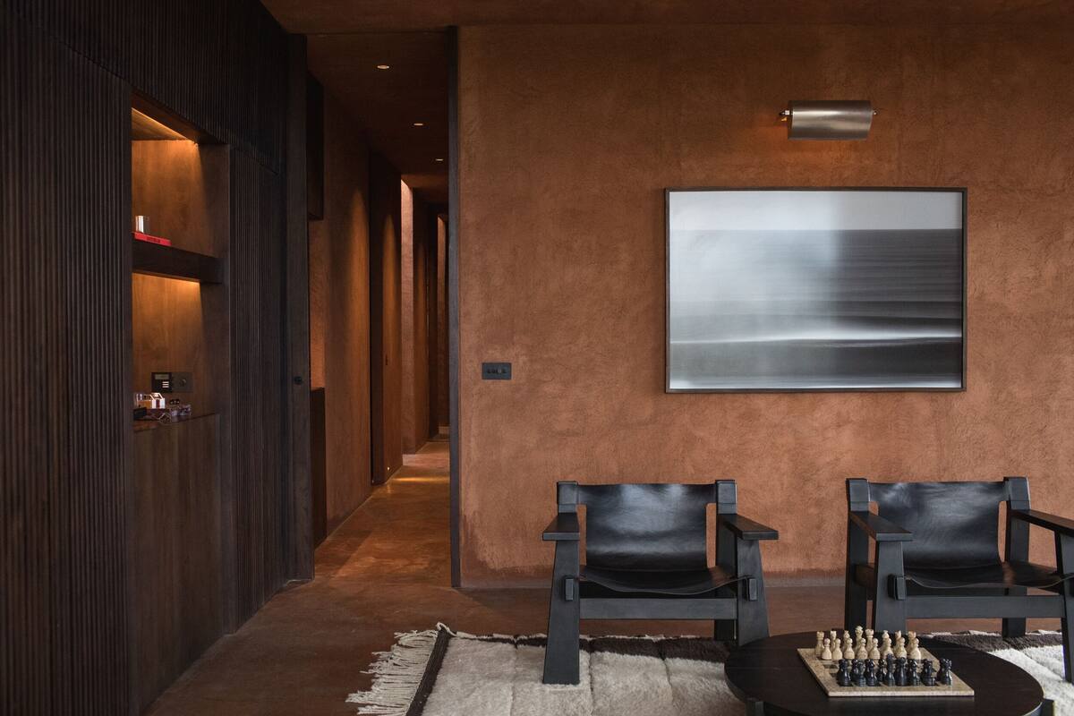 Un couloir moderne avec un mur en bois, une grande peinture abstraite et deux fauteuils en cuir accompagnés d’un jeu d’échecs.