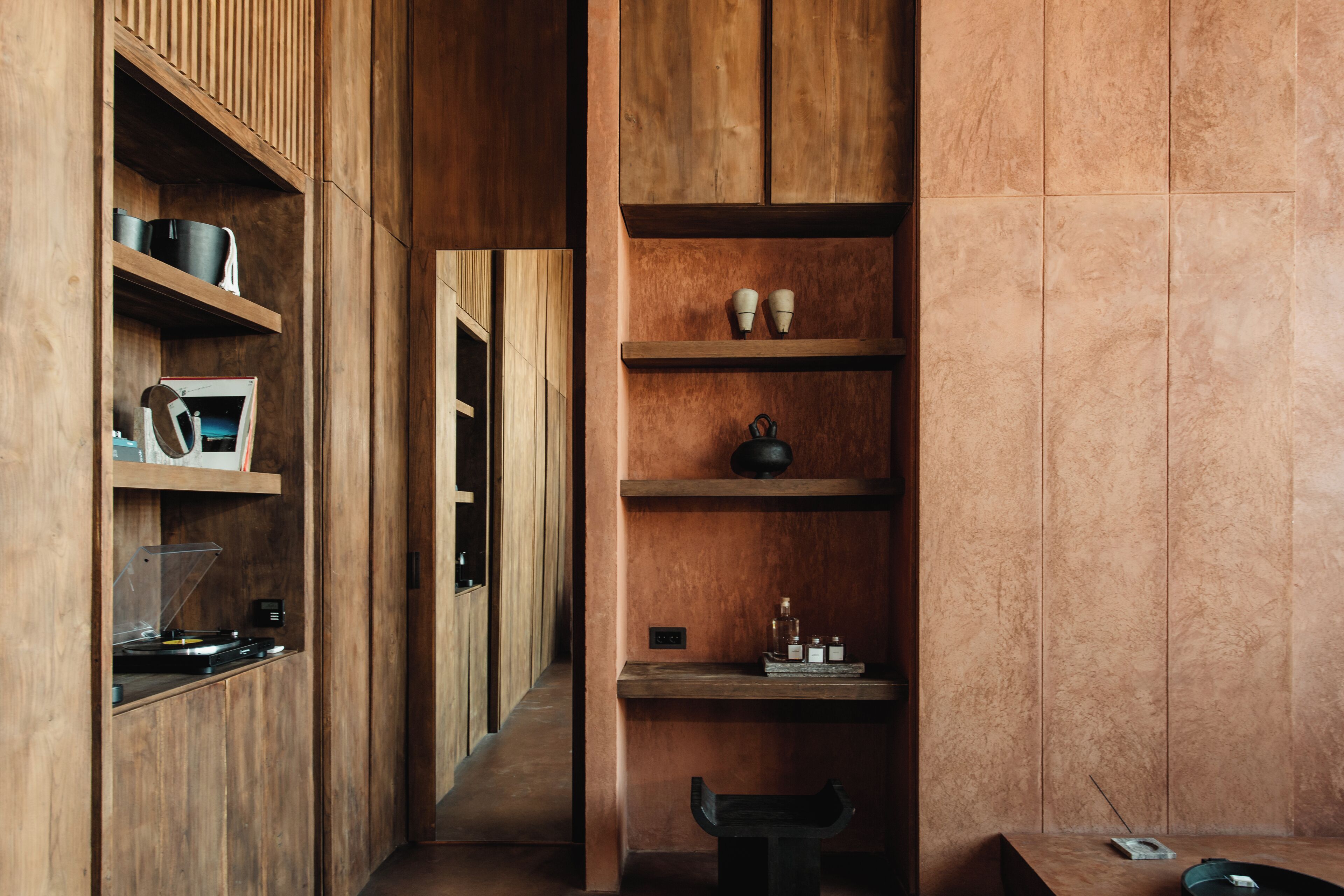 A narrow hallway with wooden shelving units on both sides, displaying various items like cups, a kettle, and a record player.