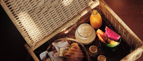 Una cesta de mimbre con pan, un vaso de zumo de naranja, un cuenco de fruta y un tarro de miel.