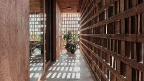 A corridor with a wooden lattice partition, a concrete floor, and a large potted plant. - Further Hotel (Pererenan)